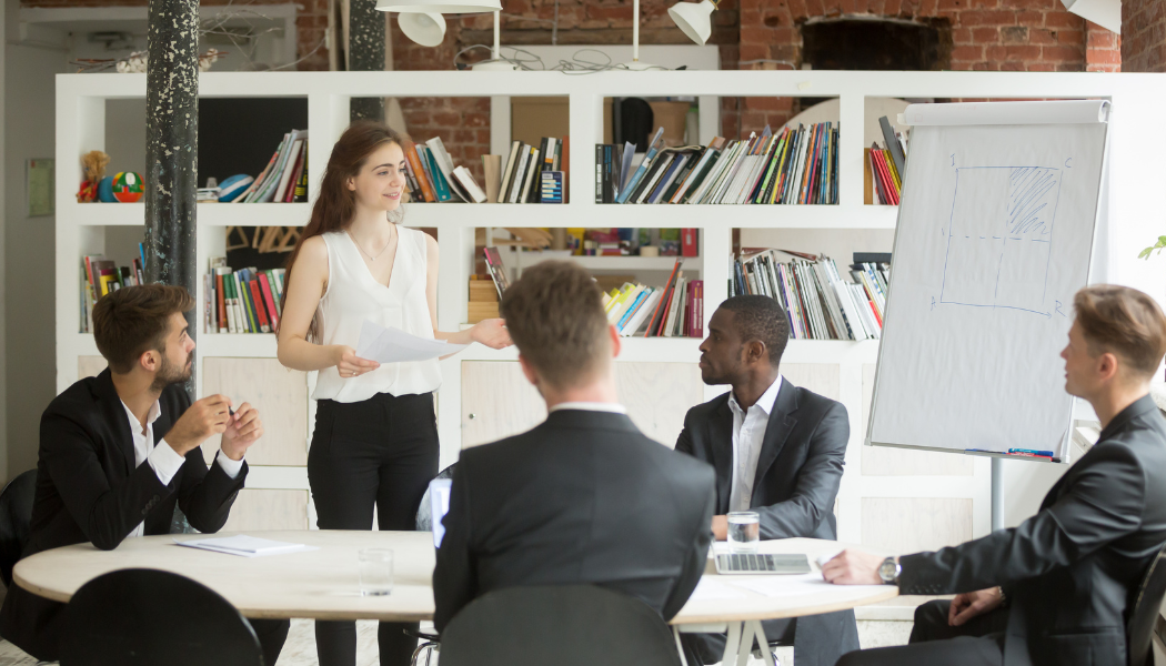 femme debout qui parle à quatre hommes assis en face d'elle